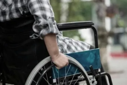 Una persona sostiene una silla de ruedas con otra persona sentada; no se ven sus rostros.