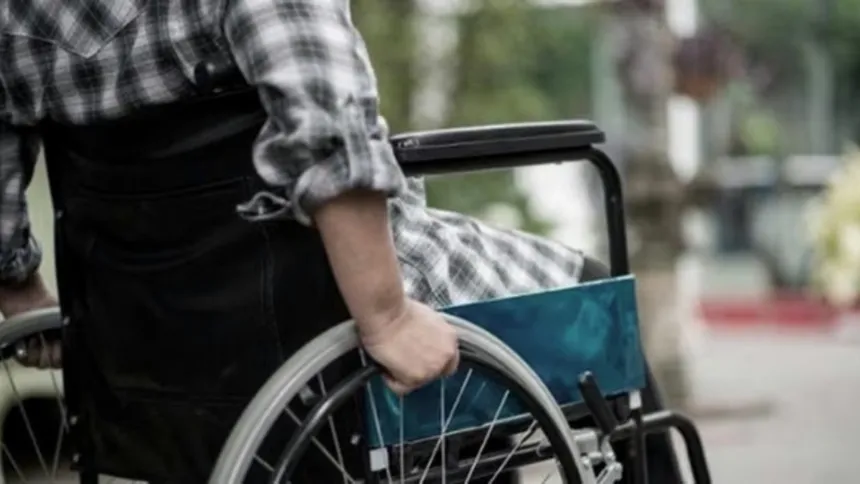 Una persona sostiene una silla de ruedas con otra persona sentada; no se ven sus rostros.