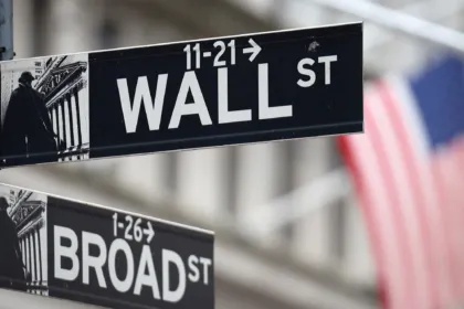 Carteles de Wall Street y Broad Street frente a una bandera estadounidense.