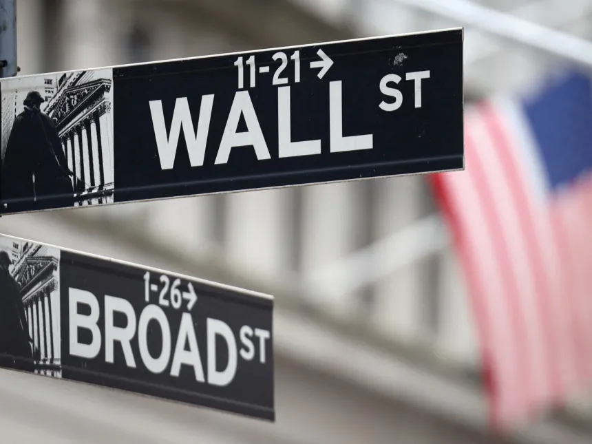 Carteles de Wall Street y Broad Street frente a una bandera estadounidense.