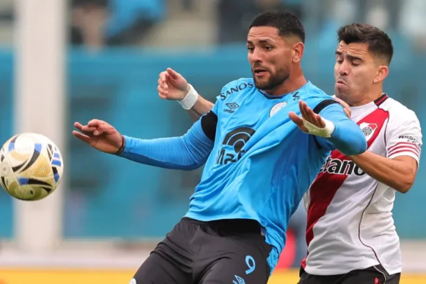 Un jugador de Belgrano disputa la pelota con un futbolista de River.