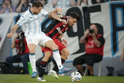 Un jugador de Racing y otro de River disputan la pelota en el campo.