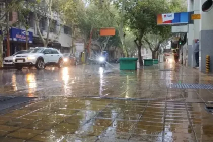 Lluvia en una calle con autos y veredas mojadas.
