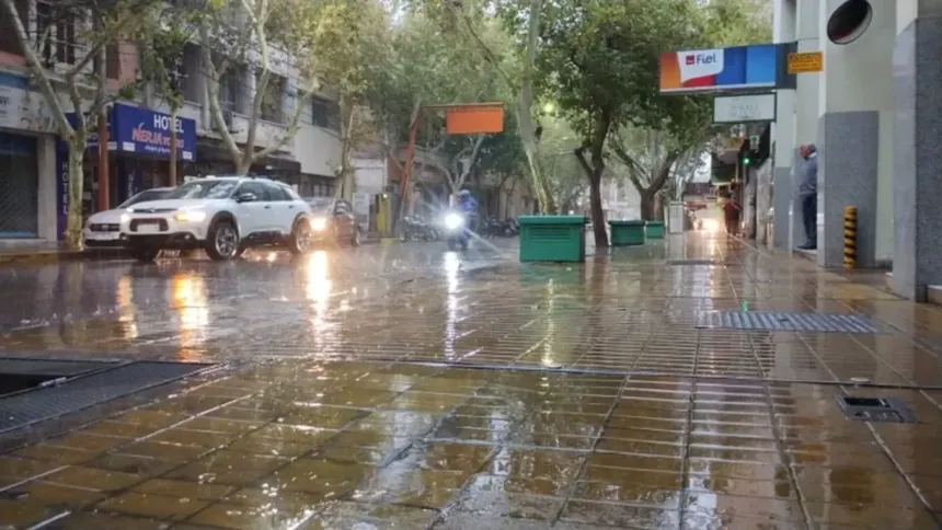 Lluvia en una calle con autos y veredas mojadas.