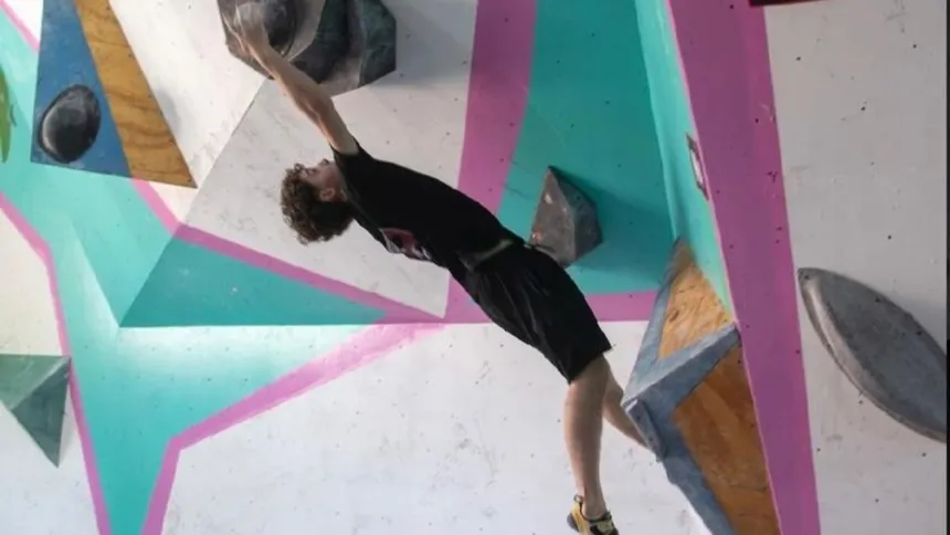Un deportista escala un muro de boulder con presas de distintos colores.