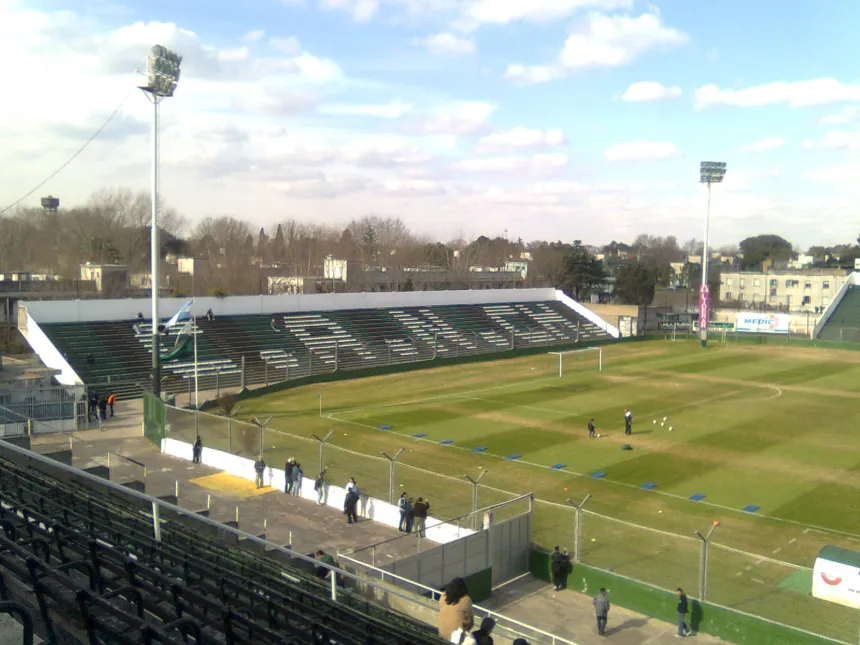 Cancha de Nueva Chicago, con tribunas verdes y negras y el campo de juego.