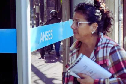 Una mujer adulta con papeles frente a un cartel de ANSES.