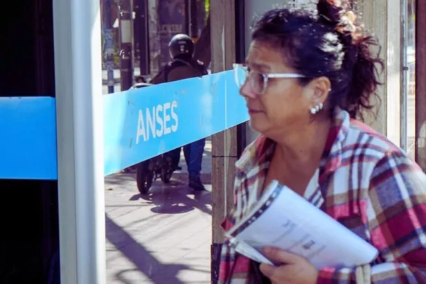 Una mujer adulta con papeles frente a un cartel de ANSES.