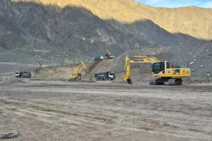 Excavadoras y camiones trabajan en un terreno árido entre montañas.