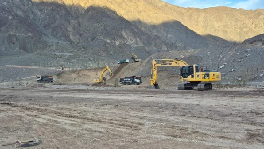 Excavadoras y camiones trabajan en un terreno árido entre montañas.