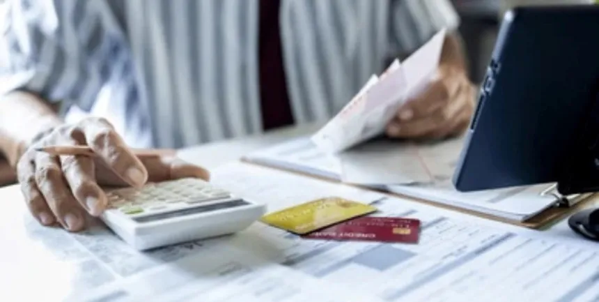 Una persona hace cuentas con una calculadora, boletas y tarjetas de crédito sobre la mesa.