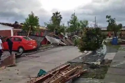 Escombros y cercos derribados en una calle con viviendas dañadas tras el tornado.
