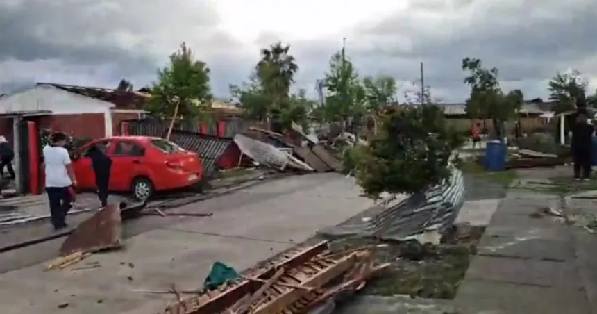 Escombros y cercos derribados en una calle con viviendas dañadas tras el tornado.
