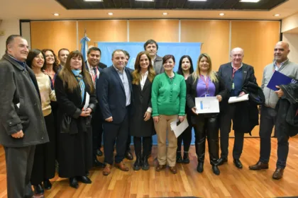 Un grupo de adultos posa en una sala y algunas personas sostienen documentos.