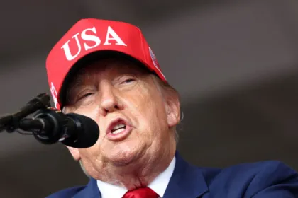 Donald Trump habla ante un micrófono y lleva una gorra roja con la inscripción «USA».чик