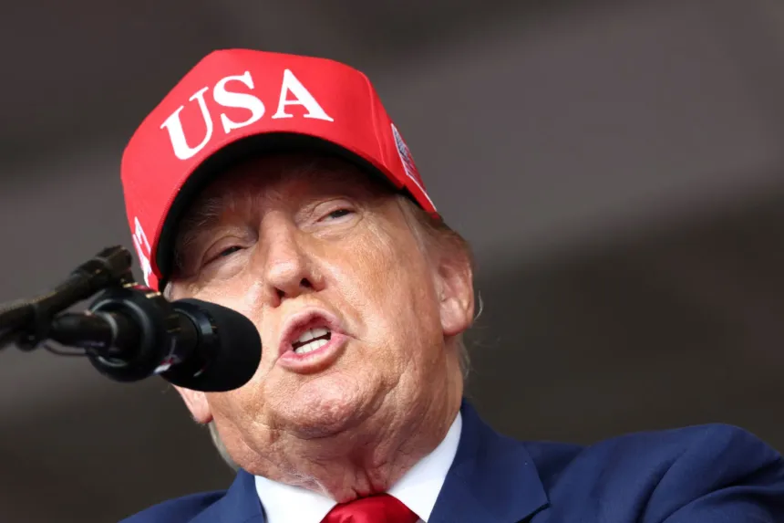 Donald Trump habla ante un micrófono y lleva una gorra roja con la inscripción «USA».чик