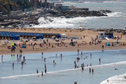 Personas disfrutan de una playa con sombrillas, carpas y olas.