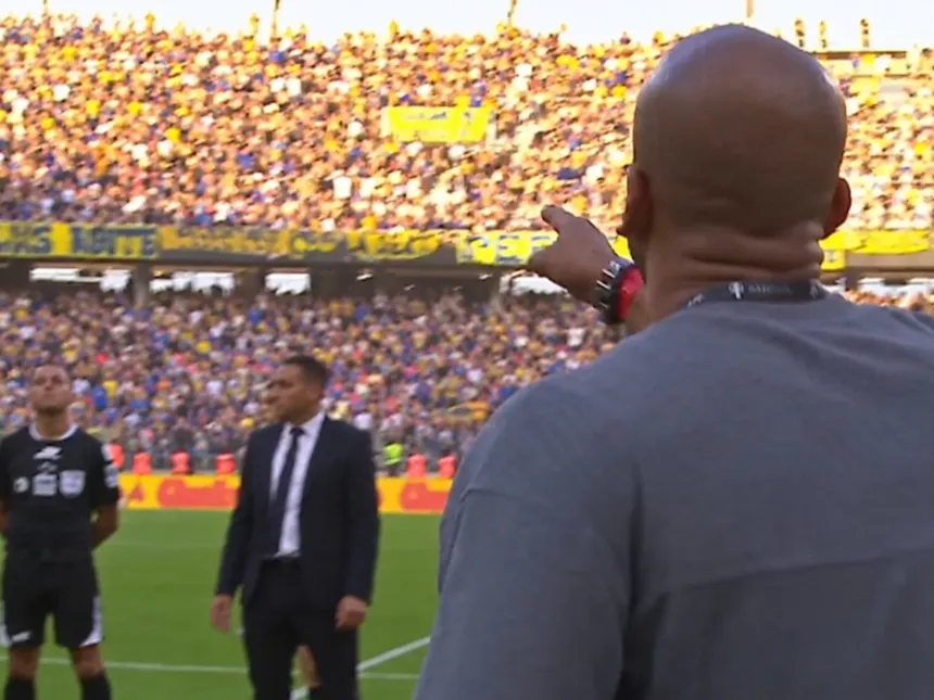 Un hombre señala hacia la tribuna durante un partido de fútbol.