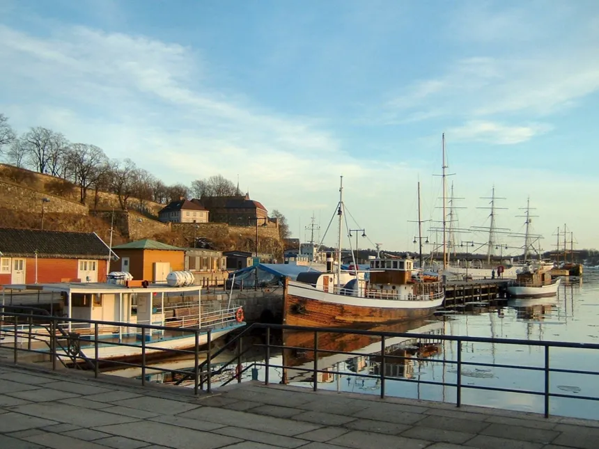 Barcos amarrados en el puerto de Oslo, junto a edificios y un paseo costero.